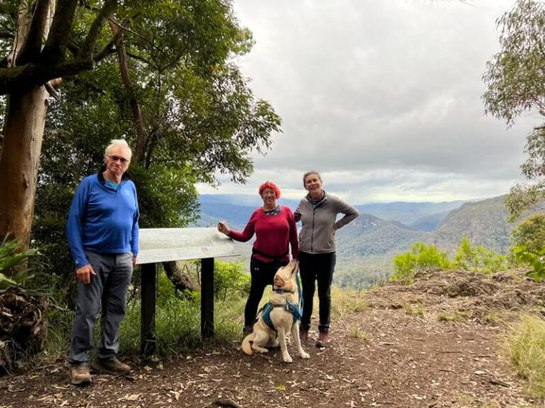 3 people and an assistance dog standing at a lookout smiling for the camera