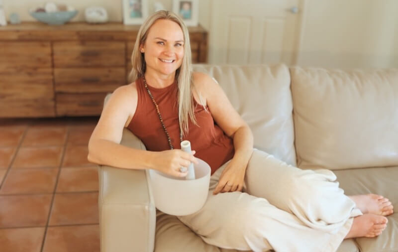 Woman on couch smiling holding a singing bowl